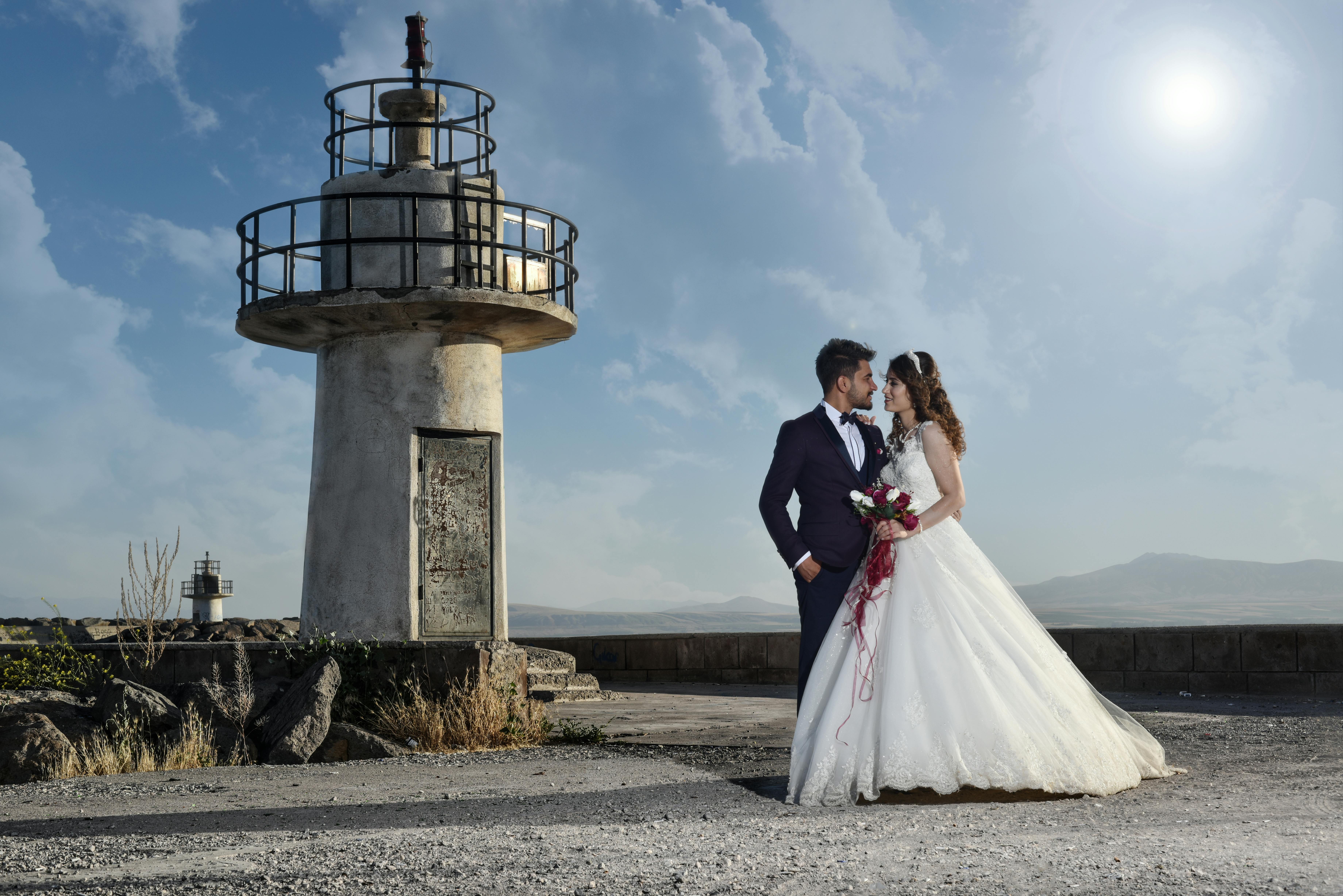 A bride and
        groom pose next to a lighthouse