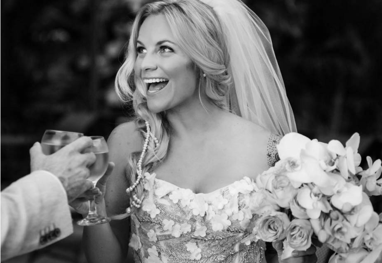 A bride toasting a glass of wine while wearing an expertly fitted dress, altered to specifically fit her body.