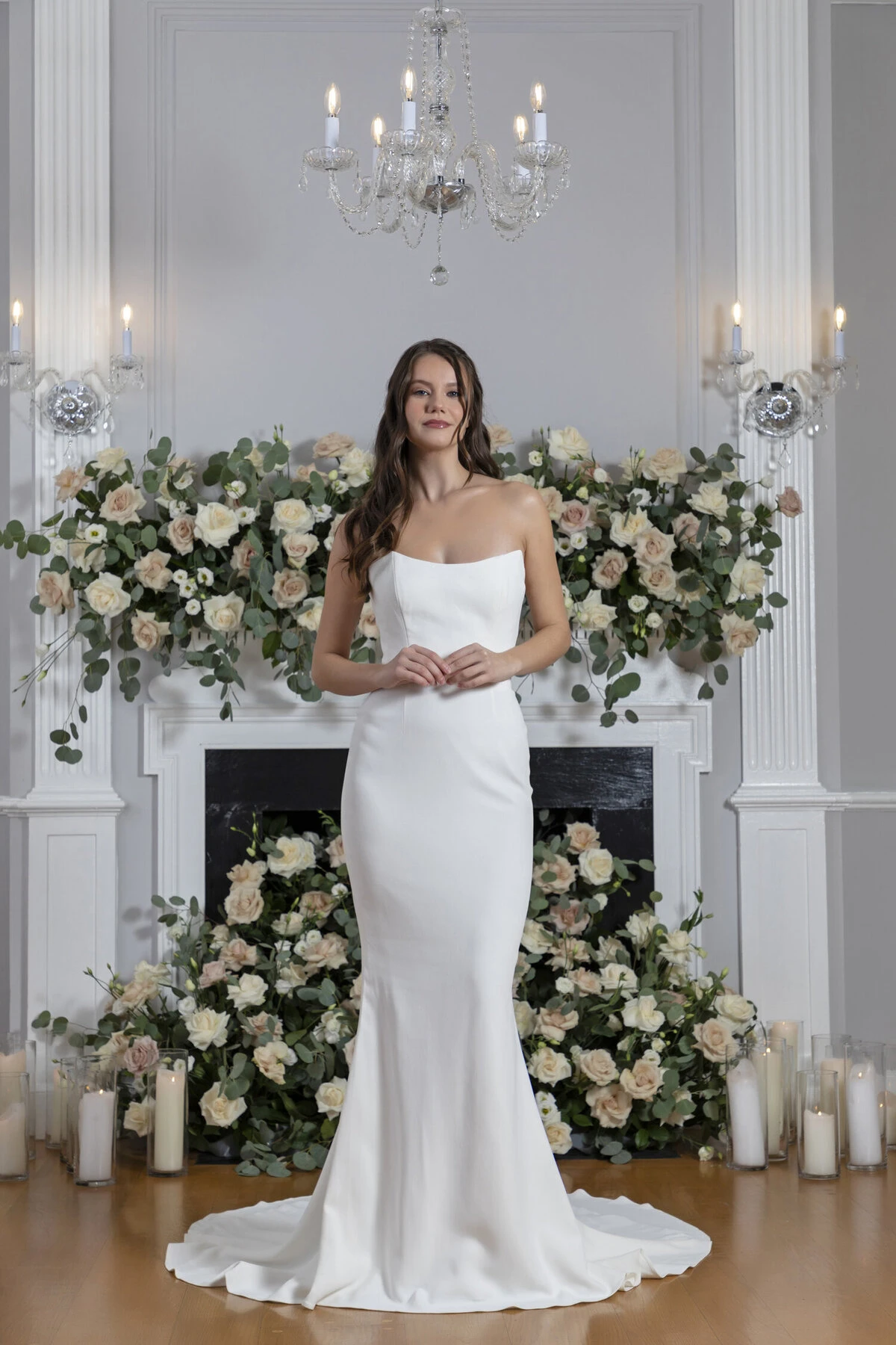 A model wears the Angel Rivera Aster dress while standing in front of a fireplace with flowers