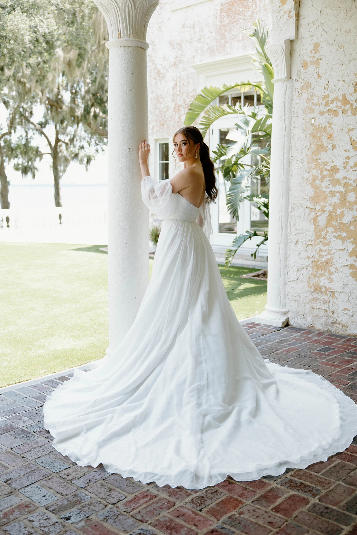 A model wears the Angel Rivera Freesia dress while leaning against a decorative pillar