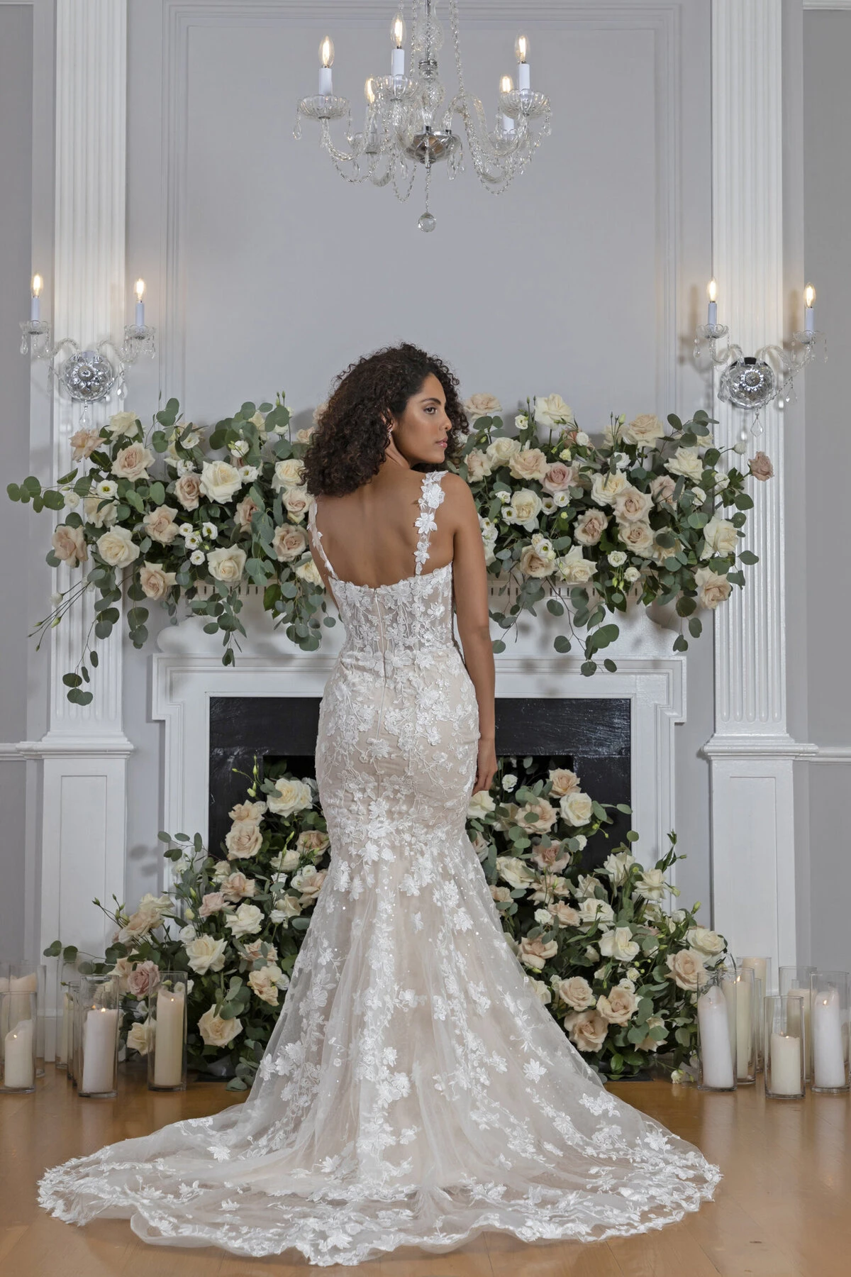 A model wears the Angel Rivera Venetian dress in front of a fireplace with flowers