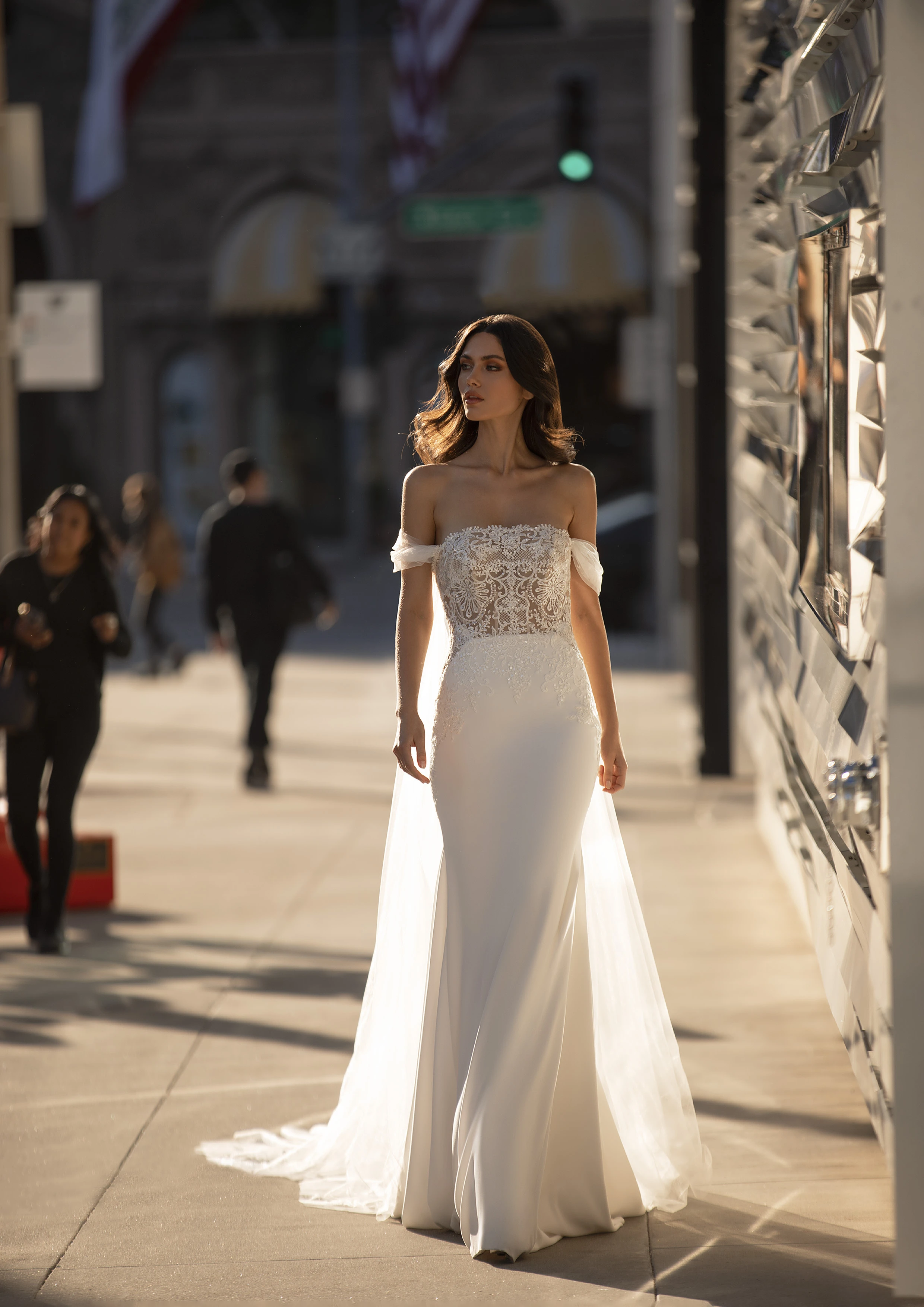 A model wears the Pronovias Novak dress while walking on downtown sidewalk